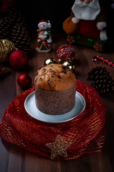Tahta bir masanın üzerinde kırmızı tülle sarılı beyaz bir tabakta panettone Noel süslemesi yayılmış..