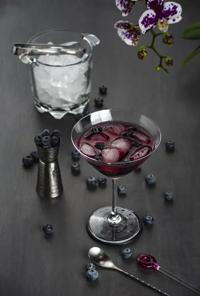 Bardakta kokteyl, yabanmersini meyvesi, orkide çiçeği, buz kovası, koyu gri arka plan. Odaklanmayı seç.