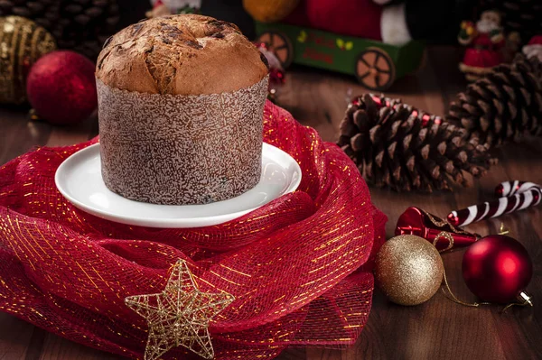 Panettone beyaz bir tabakta, noel süslemesi ahşap bir masaya rastgele dizilmiş. Boşluğu kopyala.