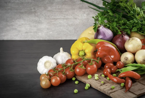 Siyah ahşap masanın yemek geçmişi. Yemek pişirmek için gerekli malzemeler - kiraz domates, soğan, patates, kırmızı ve sarı biber, bezelye ve sarımsak. Boşluğu kopyala..