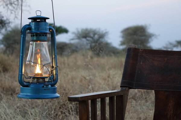 TANZANIA, SERENGETI, OLD LAMP AND CHAIR WITH SAVANNAH BACKGROUND.