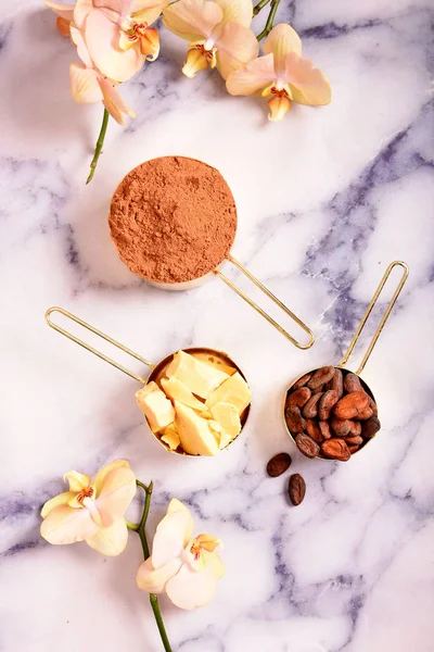 Cocoa, cocoa butter and cocoa beans, chocolate in gold containers on a marble surface. Flat lay. Place for text.