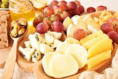 Peynir, bej bir arka planda yer alan bir plakaya yerleştirilir. Peynirler farklı türleri: Camembert, parmesan, mavi peynir, zeytin, bal, üzüm.