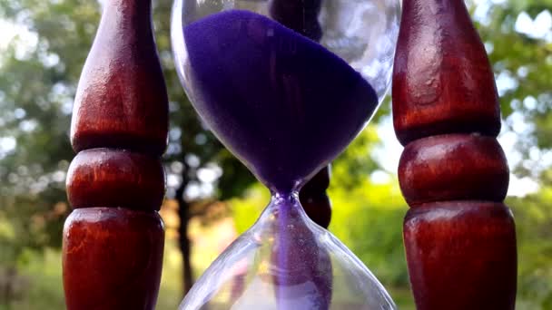 Vintage hourglass with blue sand pouring on nature background — Stock Video