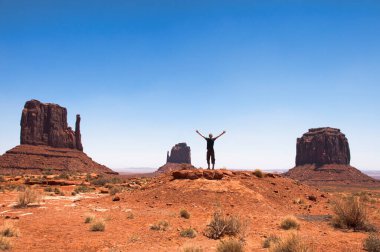 Ünlü kumtaşı popolarından bazıları Utah, ABD 'de Colorado Platosu' nun bir bölgesi olan Monument Valley 'de bulunur. Manzaranın ortasında kollarını açmış genç bir adam.