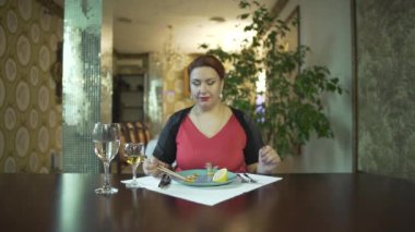 Güzel, orta yaşlı, kırmızı elbiseli bir kadın şık bir restoranda tek başına yemek çubuklarıyla yemek yiyor.