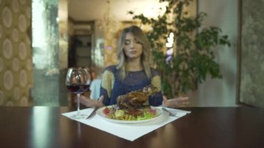 Çekici dövmeli genç bir kız süslü restoranda büyük bir parça kızarmış et yemek için bekliyor.