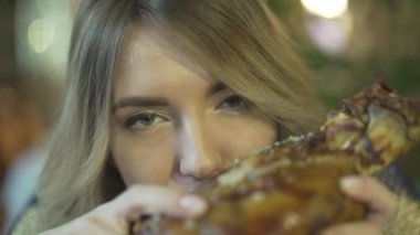 Sarışın, yakışıklı, aç gözlü, koca et parçalarını ısıran, elleri kızgın ve uygunsuz bir şekilde yemek yiyen bir kadın.