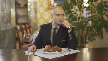 Klasik takım elbiseli, zeki, çekici ve kel bir adam. Elinde yemek bardağı kırmızı şarapla şık bir restoranda masada tek başına oturuyor.