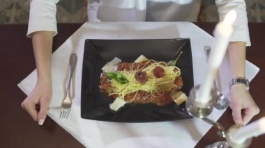 Kadın eli yakın çekimde İtalyan mutfağından makarna yerken siyah tabaktan siyah köfte yerken şık bir restoranda.