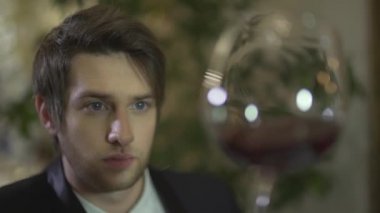 Genç, yakışıklı, esmer, mavi gözlü adam kırmızı şarabı tadıyor. Cama bakıyor ve lüks restoranda tek başına yemeğin tadını çıkarıyor.