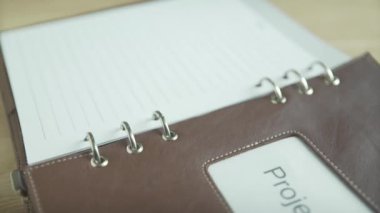 Yakın plan, zarif iş projesi not defteri günlük günlük günlük, kahverengi deri çantalı, ahşap masadaki kurşun günlük.