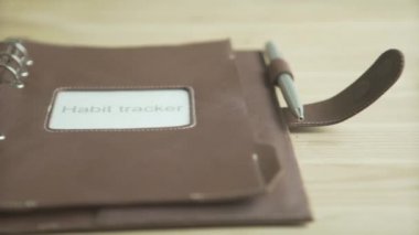 Kadın eli açık kahverengi deri çanta kullanıyor. Zarif günlük planlayıcı not defteri. Ahşap masa üzerindeki not defteri takip cihazı.