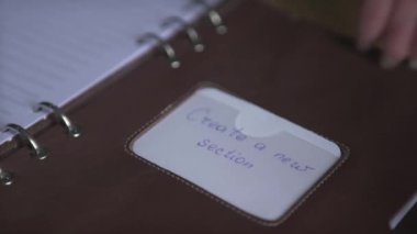 Açık kahverengi deri not defteri kullanan kadın eli. Günlük etiket yapıştırıcısı. Ahşap masaya yakın plan.