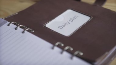 Kadın eli, kahverengi deri defter etiketli, kurşun günlük planlayıcısının fotoğrafını çek.