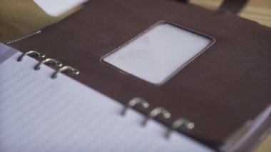 Kadın ellerinin kahverengi deri kurşun günlüğündeki etiket etiketini kullanırken yakın plan çekimleri. Günlük not defteri takip cihazı.