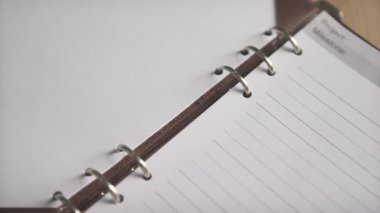 Kadın eli, deri kapak organizatörü günlük not defterinde metal klasörü açarken yakın plan.
