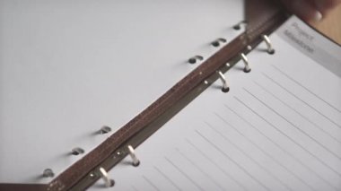 Kadın eli, deri kapaktaki çelik klasörü açıyor. Günlük planlamacımız. Not defterimiz.