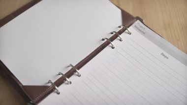 Kadın eli, deri kaplı defter defterindeki metal klasörü açıyor. Günlük planlama dergisi.