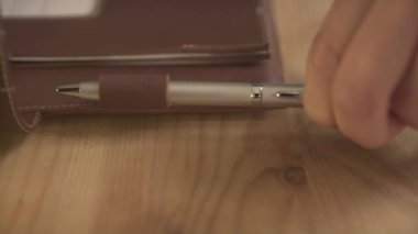 Yakın plan kadın eli, gümüş çelik kalemi deri düzenleyici günlük not defteri tutacağı ahşap masaya koyuyor.