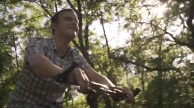 Sakin, orta yaşlı, ekose gömlekli, güneşli yaz gününde boş bir caddede yavaş bisiklet süren bir adamın düşük açılı çekimi.