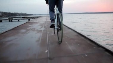 Pembe günbatımında nehir kenarında bisiklet süren genç bir adam, sağlıklı bir açık hava yaşam tarzı.