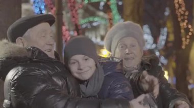 Mutlu, yaşlı, evli çift, torunu kucaklıyor Noel ışığında aydınlatma gecesinde.