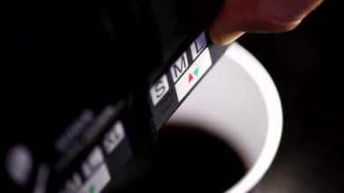 Plastik bardakta köpüklü soda doldurmak için otomatik içecek makinesi kullanan bir adamın 4k değişen odak fotoğrafını kapat.