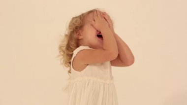 Sevimli, küçük, şirin, kıvırcık saçlı, beyaz elbiseli, saklambaç oynayan küçük kız.