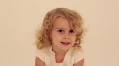 Sevimli, küçük, şirin kıvırcık saçlı, beyaz elbiseli, heyecanlı bir şekilde kameraya atlayan küçük kız çocuğu.