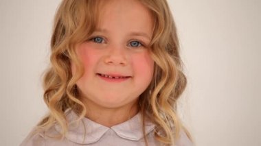 Küçük, şirin, küçük bir kız çocuğunun, pembe yanaklı, kıvırcık saçlı ve kamerada gülümseyen bir fotoğrafını yakın plan çekelim.