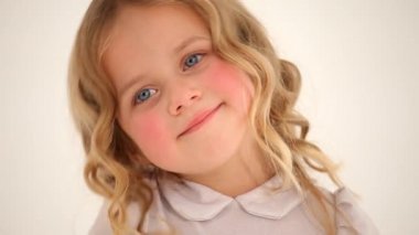 Kıvırcık sarı saçlı, pembe yanaklı, kameraya gülümseyen şirin, küçük, güzel bir kız çocuğunun yakın plan fotoğrafı.