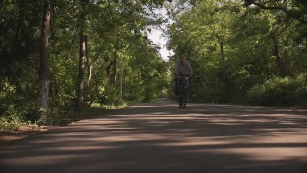 夏日阳光明媚 一个快乐的中年男子骑着自行车穿过绿树公园 在空旷的自行车道上拍摄的低角度照片 — 图库视频影像