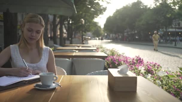 Joven Mujer Rubia Vestido Blanco Terraza Cafetería Exterior Escribiendo Pensamientos — Vídeos de Stock