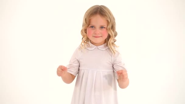 可愛いです少し恥ずかしがり屋小さな素敵な幼児女の子子供とともにブロンド巻き毛でホワイトドレス描画大心で空気中で指 — ストック動画