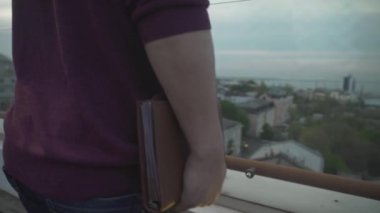 Kuş bakışı manzarayı kapat. Koyu saçlı adam çatıda ayakta duruyor. Hayal kuruyor, deniz kenarı limanına bakıyor.