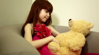 Sevimli küçük mutlu kız sakin çocuk sandalyede oturmuş büyük pelüş pelüş oyuncak ayısına bakıyor.