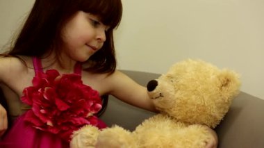 Küçük tatlı, mutlu, sakin çocuk sandalyede oturmuş peluş oyuncak ayısına bakıyor.