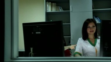 İki bilgisayar ekranının arkasında oturan genç, güzel kadın doktor gülümseyen, heyecanlı, parmağını gösteren küçük bir kız.