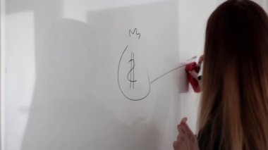 Genç, güzel, uzun saçlı bir kadın siyah keçeli kalemle beyaz tahtaya resim çiziyor.