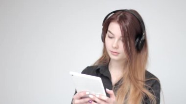 Kulaklık takan güzel bir genç kız beyaz tablet kullanıyor.