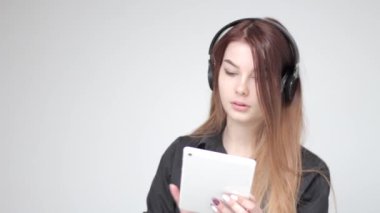 Kulaklıklı, beyaz tabletle oynayan genç ve güzel bir bayan fotoğraf çekiyor.