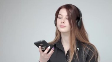 Kulaklıklı genç bir kadın akıllı telefonlu bir selfie için poz veriyor.