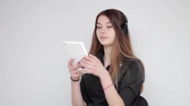 Beyaz tablette kablosuz kulaklık dinleyen mutlu, genç bir kadın.