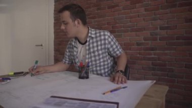 Ekose gömlekli, genç, kendine güvenen, iş projesinde çalışan, ahşap masada oturan çekici bir adam.