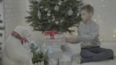Mutlu küçük çocuk Noel hediyesi kutusunu süslenmiş yeni yıl ağacı şenlikli atmosfer odasında açıyor.
