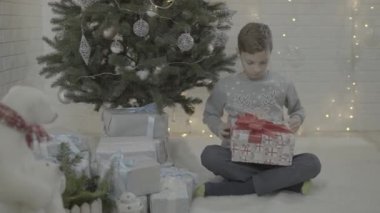 Küçük mutlu çocuk Noel hediyesi kutusunu dekore edilmiş yeni yıl ağacı şenlik atmosfer odasında açıyor.