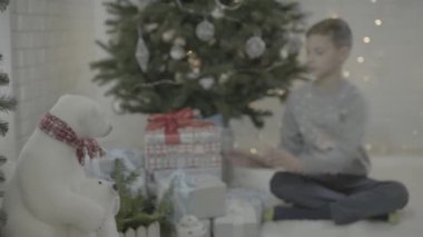 Heyecanlı küçük çocuk Noel hediyesi kutusunu dekore edilmiş yeni yıl ağacı şenlikli atmosfer odasında açıyor.