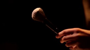 Makyaj malzemesi tutan, temeli kızartan, barut kalıntılarını silkeleyen kadının koyu arkaplan çekimini kapat.