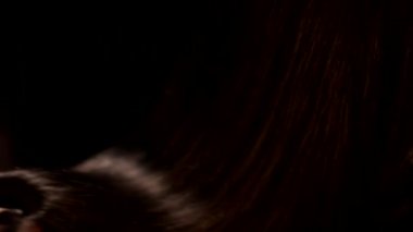 Siyah arka plan, kadın elinin dönüşümlü güzel, düz, esmer, koyu renkli, parlak saçlarının yakın plan çekimi.